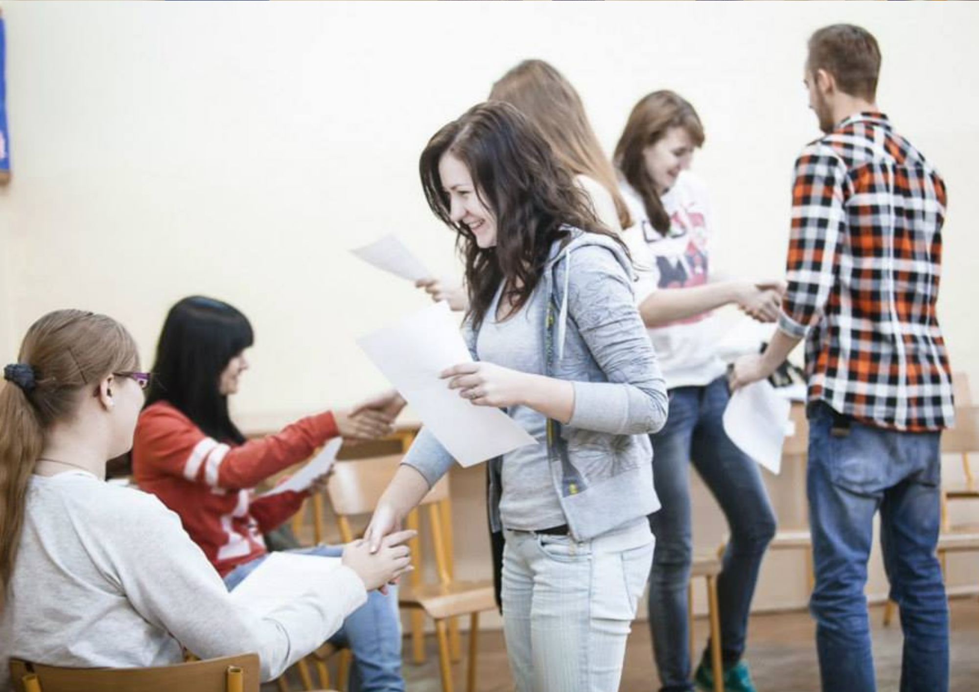 Zdjęcie osób które przekazują sobie kartkę - być może dyplom i podają sobie dłonie.