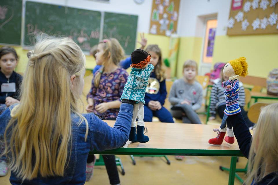Dwójka dzieci odgrywająca scenkę pacynkami - w tle rozmazane siedzące pozostałe dzieci patrząca na odgrywaną scenkę