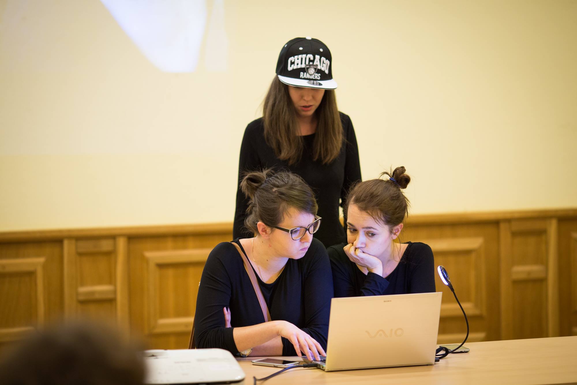 Zdjęcie wykonane podczas spektaklu Teatru Forum. Przedstawia trzy aktorki patrzące na komputer.