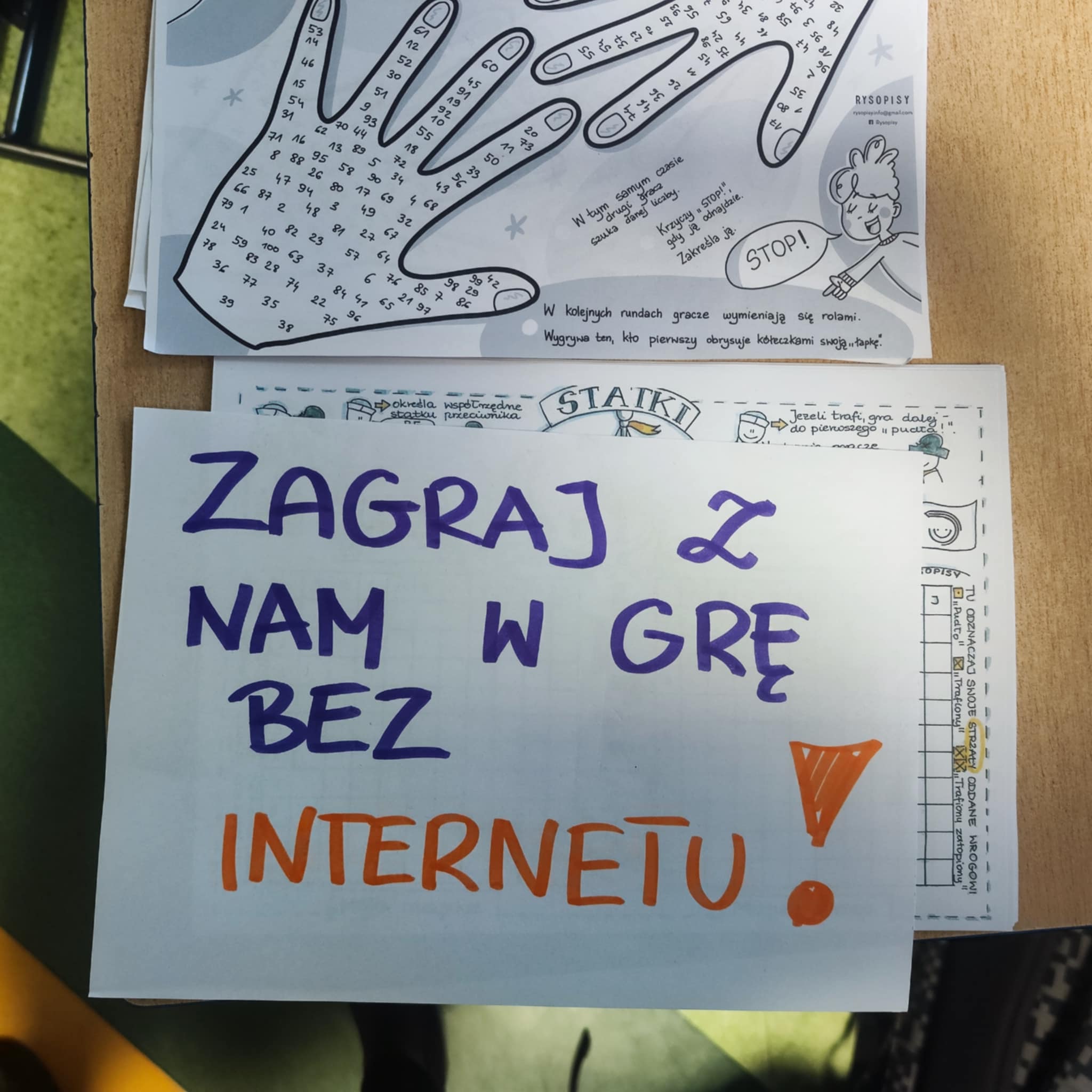 Rozłożone na stoliku gry w statki i w łapki oraz kartka “Zagraj z nami w grę bez internetu”.
